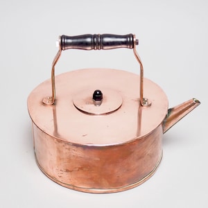 Könnte beinhalten: Ein Kupferkessel mit einem schwarzen Holzgriff und einem schwarzen Knopf auf dem Deckel.