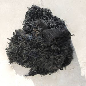 May include: A black, shaggy, textile sculpture made from recycled materials. The sculpture is made of long, thin strips of fabric that are woven together to create a three-dimensional form.