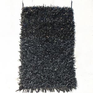 May include: A black shaggy rug made from recycled materials. The rug has a long, frayed fringe on all sides.