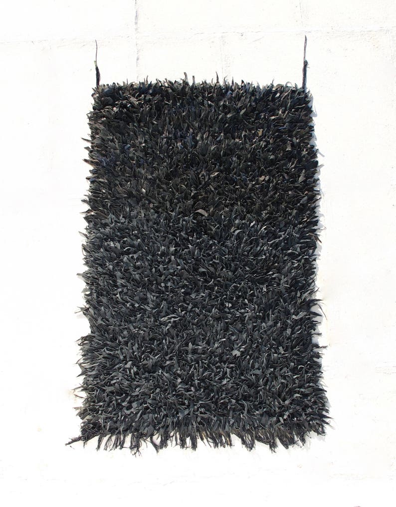 May include: A black shaggy rug made from recycled materials. The rug has a long, frayed fringe on all sides.