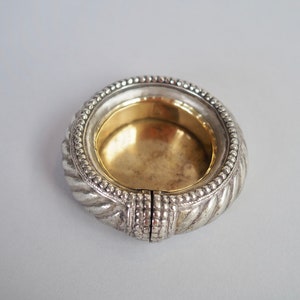 Puede incluir: Un posavasos circular de plata y oro con un diseño decorativo de cuerda alrededor del borde.