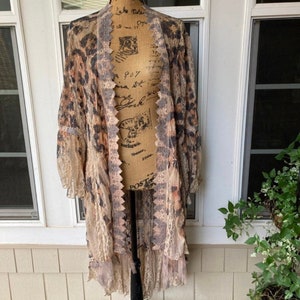 May include: A long, sheer, beige and brown leopard print cardigan with lace trim and a ruffled hem.