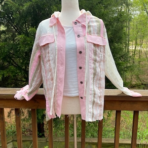 May include: A pink and white striped button-up shirt with a hood. The shirt has a frayed hem and is made of a lightweight fabric.