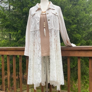 May include: A long, cream-colored denim jacket with a lace overlay. The jacket has a button closure and two pockets. The lace overlay is white and has a floral pattern.