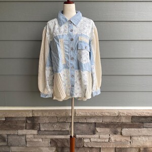 May include: A light blue patchwork shirt with a floral print and crochet detailing. The shirt has a button-up front and long sleeves.