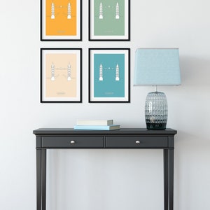 May include: Four framed prints of the Tower Bridge in London, each with a different background color: yellow, green, beige, and blue. The prints are hanging on a white wall above a black console table with two drawers. A blue lamp with a clear glass base is on the table.