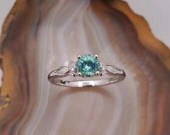 May include: A silver ring with a round, light blue and green gemstone surrounded by two smaller, clear gemstones.