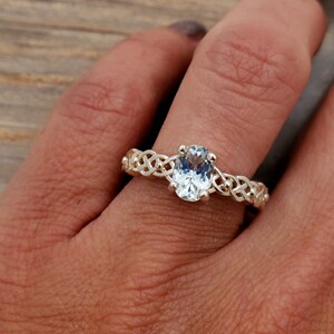 May include: A silver ring with a Celtic knot design and a clear oval-shaped gemstone.