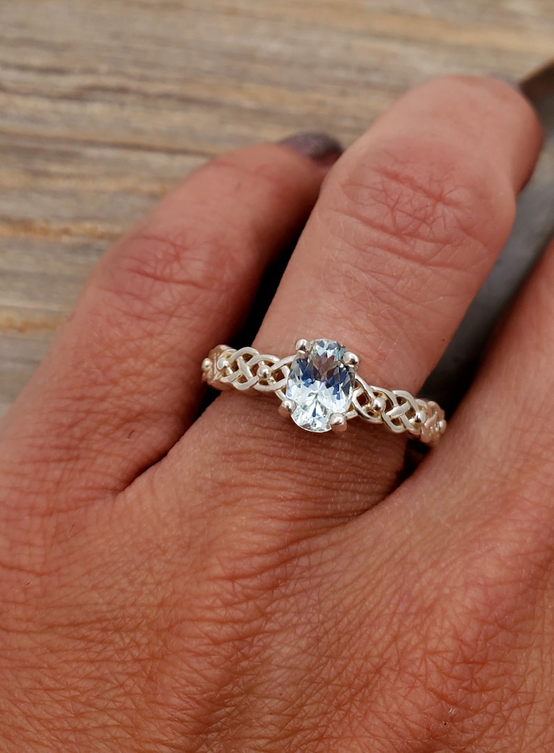 May include: A silver ring with a Celtic knot design and a clear oval-shaped gemstone.