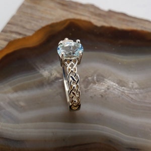 May include: A silver ring with a braided band and a light blue oval gemstone.