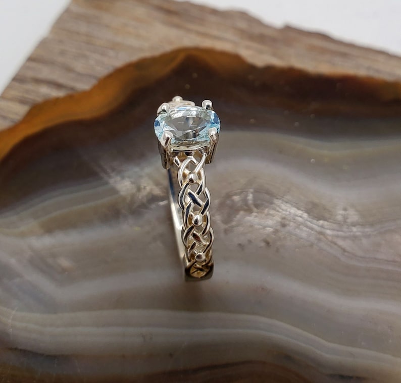 May include: A silver ring with a braided band and a light blue oval gemstone.
