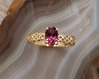 May include: A gold ring with a pink oval gemstone set in a Celtic knot design.