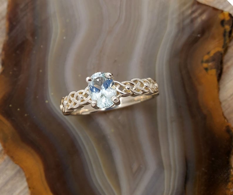 May include: A silver ring with a light blue oval gemstone set in a Celtic knot design.