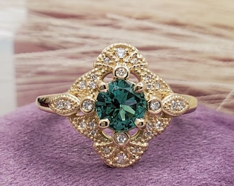 Puede incluir: Un anillo de oro con una piedra preciosa verde rodeada de pequeños diamantes en un diseño delicado e intrincado.