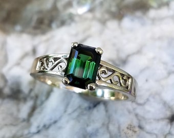 May include: A silver ring with a green emerald-cut gemstone set in a delicate filigree design.
