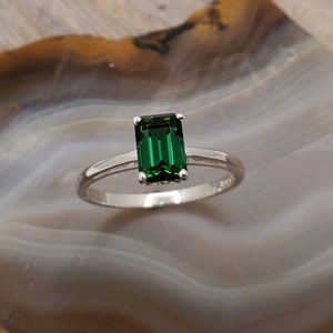 May include: A silver ring with a dark green emerald-cut gemstone.