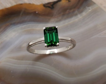 May include: A silver ring with a dark green emerald-cut gemstone.