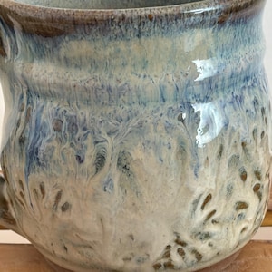Pu&ograve; includere: Una tazza in ceramica fatta a mano con una smaltatura unica. La tazza presenta una miscela di colori blu, bianco e marrone, creando un effetto marmorizzato. La tazza ha una forma arrotondata e un manico, perfetta per gustare bevande calde.