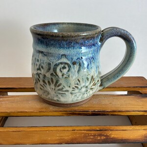 Pu&ograve; includere: Una tazza in ceramica fatta a mano con una glassa blu e bianca. La tazza presenta un motivo floreale decorativo e un grande manico. La tazza &egrave; alta circa 10 cm e ha un diametro di 9 cm.