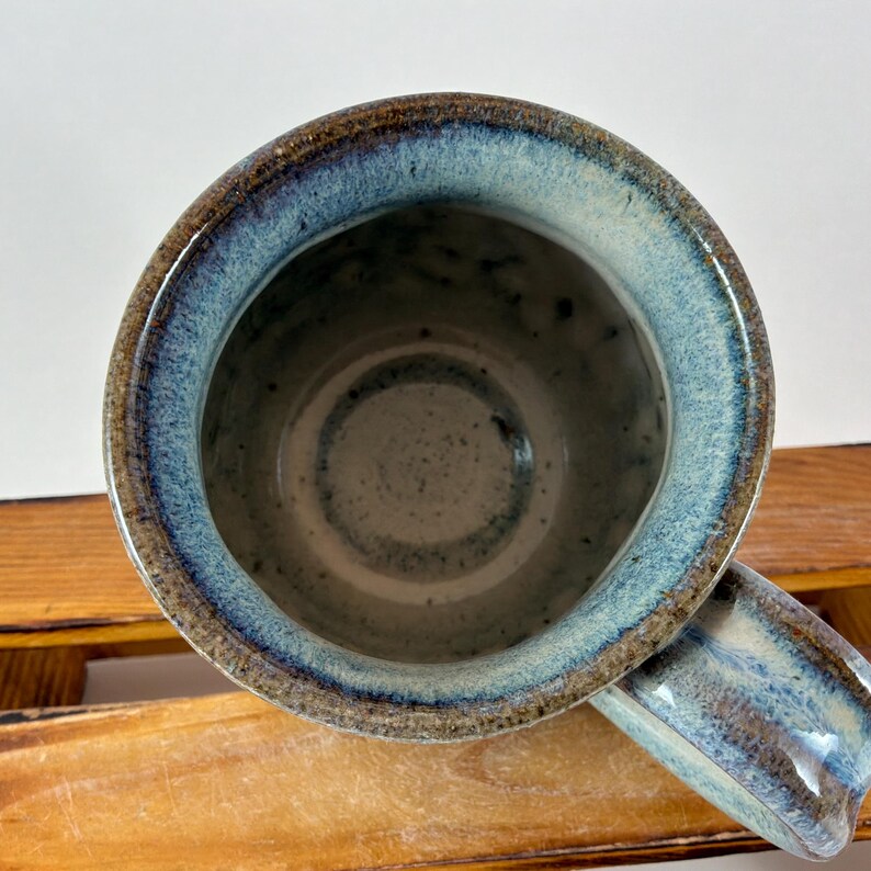 Pu&ograve; includere: Tazza in ceramica fatta a mano con una glassa blu e marrone unica. La tazza ha una forma arrotondata con un manico robusto. L'interno ha una finitura maculata, azzurra e grigia. Questa tazza artigianale &egrave; perfetta per le bevande calde.