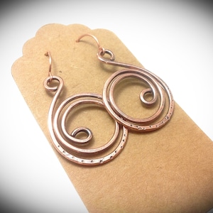 May include: A pair of copper wire earrings with a spiral design. The earrings are textured and have a hammered finish.