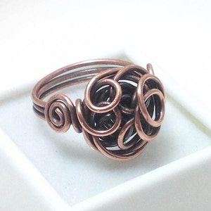 May include: A copper wire ring with a twisted, knotted design. The ring is made of multiple strands of wire that are intertwined to create a unique and intricate pattern.