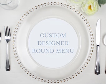 May include: A clear glass charger plate with a beaded rim and a white round card with the text "CUSTOM DESIGNED ROUND MENU" on top of it.
