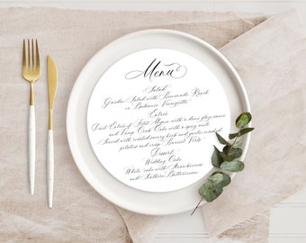 May include: A white plate with a calligraphic menu for a wedding. The menu includes a garden salad with a choice of dressings, a duet of filet mignon or crab cake, and a wedding cake with strawberries and buttercream.