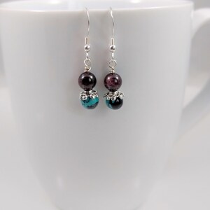 May include: A pair of silver dangle earrings with two beads on each earring. The top bead is a dark red garnet and the bottom bead is a turquoise and black agate.