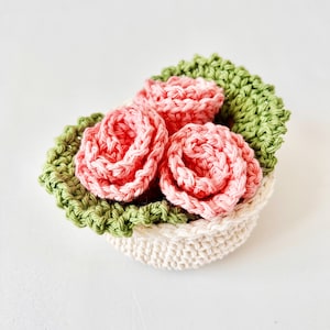Peut inclure: Un arrangement de fleurs crochetées avec trois roses roses dans un panier crème avec des feuilles crochetées vertes.