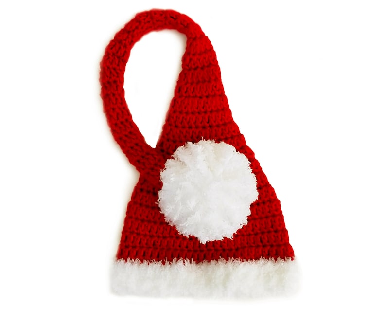 Pu&ograve; includere: Cappello di Babbo Natale rosso all'uncinetto con un pon pon bianco in cima e un bordo di pelliccia bianca intorno al fondo.
