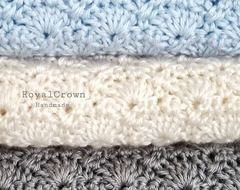Puede incluir: Tres mantas de crochet apiladas una encima de la otra. La manta superior es azul claro, la manta del medio es blanca y la manta inferior es gris. La manta del medio tiene el texto "RoyalCrown Handmade".