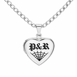 Peut inclure: Un pendentif médaillon en forme de cœur de couleur argentée suspendu à une chaîne à maillons assortie. Le devant du médaillon présente une impression graphique noire des lettres P&R dans une police gothique au-dessus d'une toile d'araignée.