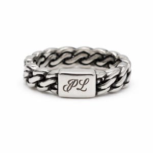 May include: A silver-toned metal ring featuring a chain-link design with a smooth, rectangular central plate. The plate is engraved with the letters PL in a cursive script font. The ring has a polished finish with darkened recessed areas.