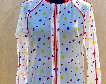 May include: A white bomber jacket with a red zipper and red trim. The jacket has a geometric pattern of red, blue, and yellow squares on a white background.