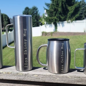 May include: Four stainless steel travel mugs with different sizes and inscriptions. The mugs are on a wooden surface. The largest mug is 30oz Skinny Mug, the next is 20oz Skinny Mug, the third is 14oz Coffee Mug, and the smallest is 14oz Camper Mug.