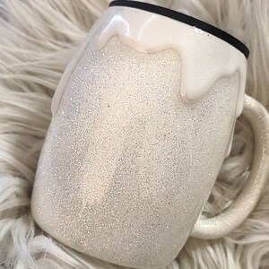 May include: White glitter tumbler with a white drip design. The tumbler has a black lid.