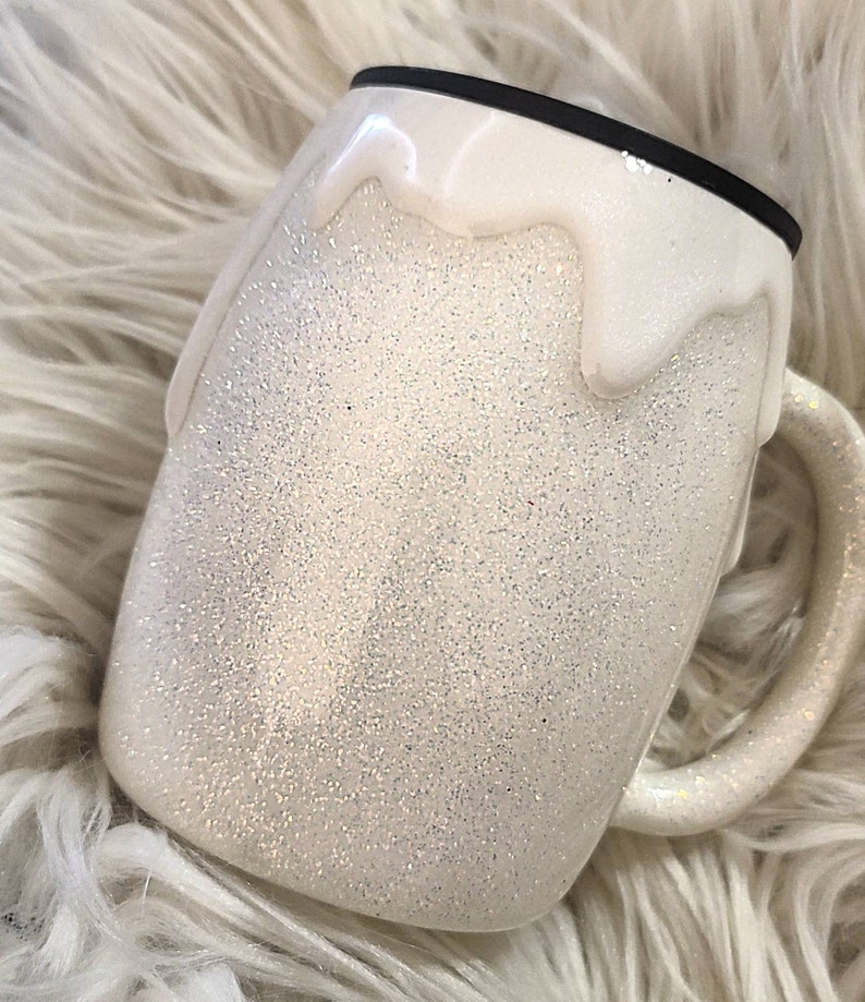 May include: White glitter tumbler with a white drip design. The tumbler has a black lid.