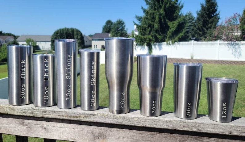 May include: A set of eight stainless steel tumblers in various sizes, ranging from 12 oz to 40 oz. The tumblers are all silver and have different size labels on them, including "12oz", "20oz", "30oz", "20oz Skinny", "30oz Skinny", "40oz", and "30oz Thick".