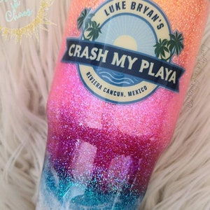 May include: A pink and blue glitter tumbler with a white and blue beach scene and the text "LUKE BRYAN'S CRASH MY PLAYA RIVIERA CANCUN, MEXICO".