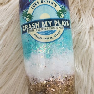May include: A blue and white tumbler with glitter. It features a graphic of palm trees and the text "Luke Bryan's Crash My Playa January 19-22, 2023 - 4 Nights of Music Riviera Cancun, Mexico".
