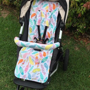 May include: A black stroller with a white and colorful feather patterned seat liner. The stroller has a black canopy and black wheels.