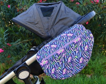Könnte beinhalten: Ein lila und blauer Kinderwagen-Organizer mit Blumenmuster und einer Reißverschlusstasche. Der Organizer ist am Lenker eines Kinderwagens befestigt.