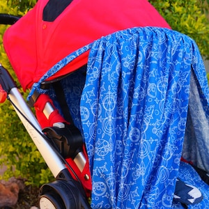 Op de afbeelding: Een rode kinderwagen met een blauwe en witte gestreepte kap. De kap heeft een geometrisch ontwerp met witte cirkels en lijnen op een blauwe achtergrond.