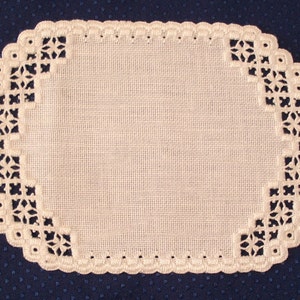 May include: A white, oval-shaped doily with a detailed, openwork lace border. The border features a repeating pattern of floral and geometric shapes. The doily is set against a dark blue, dotted background, highlighting its delicate design.