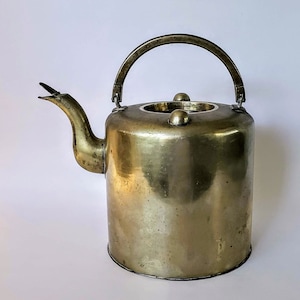 May include: A vintage brass kettle with a curved spout and a handle. The kettle has a worn, aged look and is a traditional design.