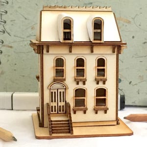 May include: A wooden model of a two-storey house with a white roof, brown trim, and a front porch with steps. The house has six windows and a double door.