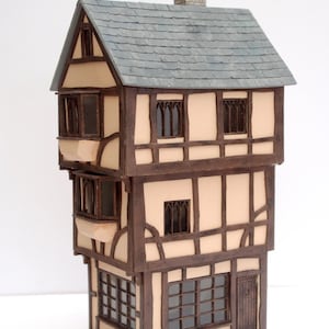 May include: A three-storey, brown and cream-coloured model house with a slate roof and a chimney. The house has multiple windows and a door. The house is made of wood and has a detailed exterior.