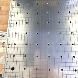 May include: A silver metal work surface featuring a grid pattern and multiple evenly spaced holes. Ruler markings with measurements in inches are visible along the edges. The Dodgers logo is present on the side.