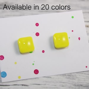 May include: A pair of bright yellow square stud earrings attached to a white display card featuring colourful polka dot accents and the text Available in 20 colours. The earrings have a smooth, glossy finish and a simple, geometric shape.